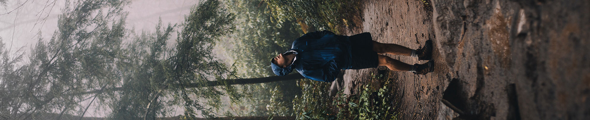 Man wearing raincoat and hiking boots looking up at the sky in a foggy forest